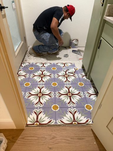 Installer laying colorful floral patterned tile in a small bathroom doorway.